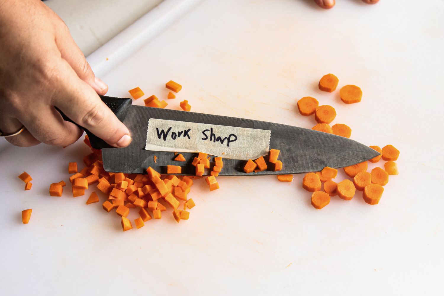A knife held over a pile of chopped carrots on a cutting board
