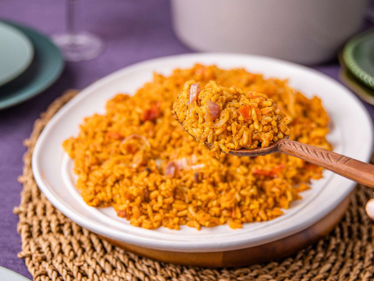 A plate of Jollof rice served on a woven mat with a spoon scooping some up