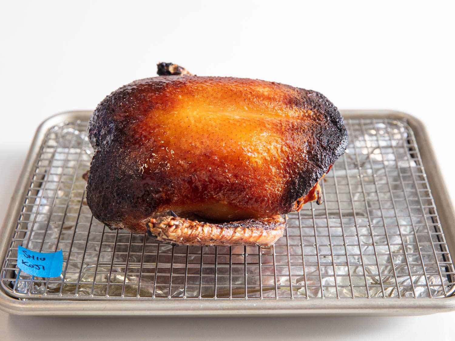 Side view of whole crown of koji roast duck on a wire rack-lined baking sheet.