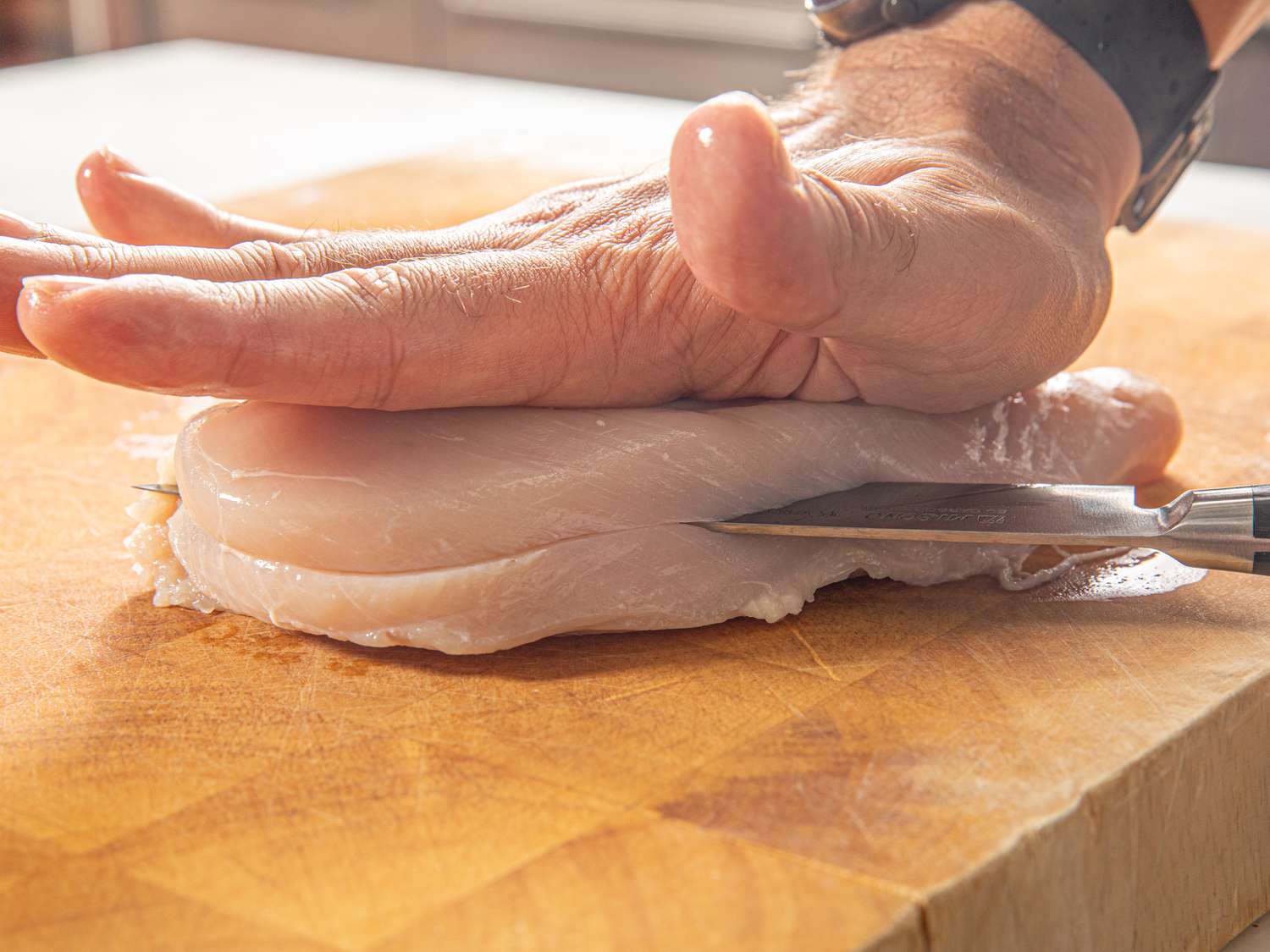 Side view of cutting a chicken breast in half. 