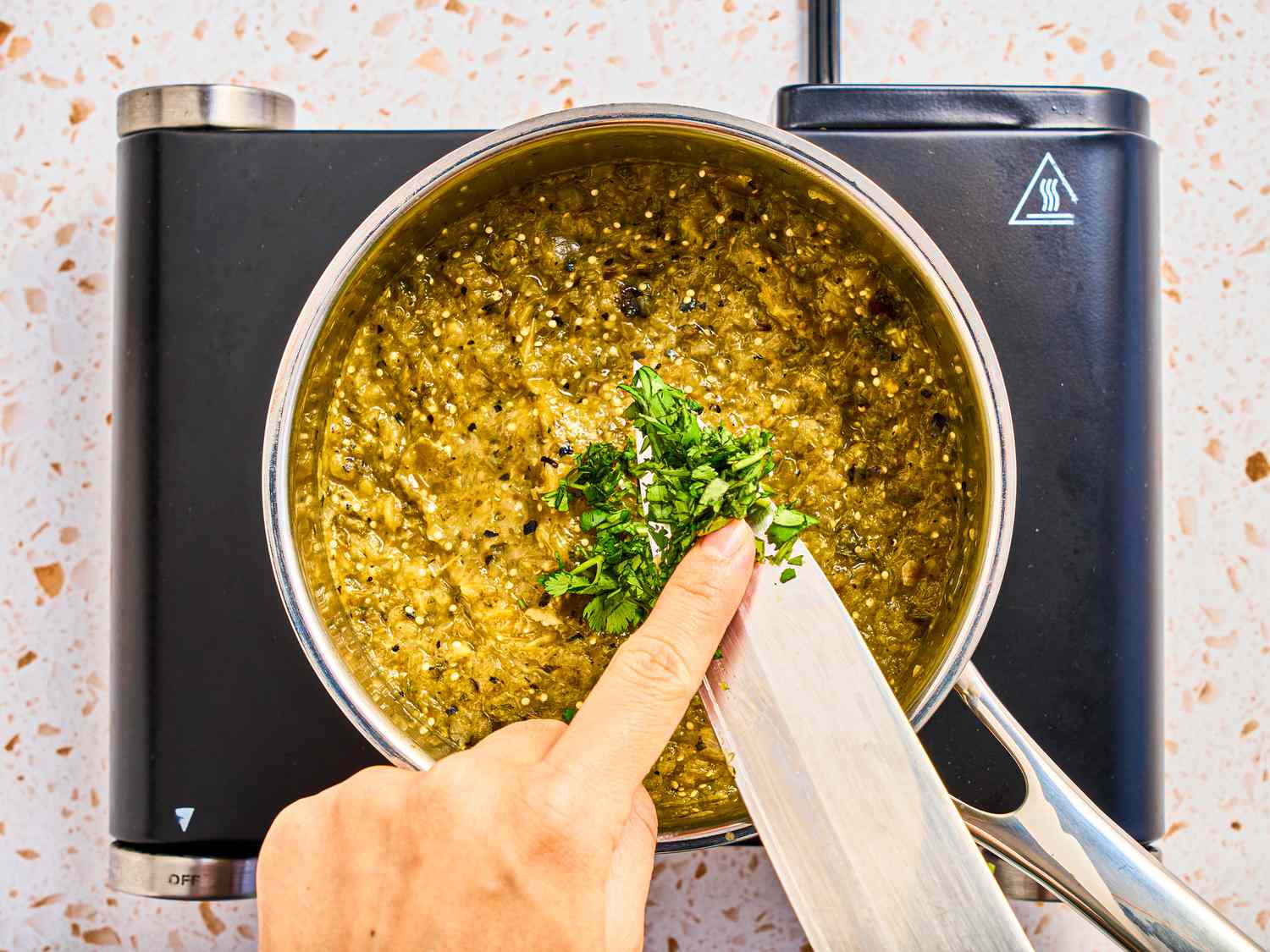 hand adding fresh chopped cilantro to into salsa on a medium saucepan 