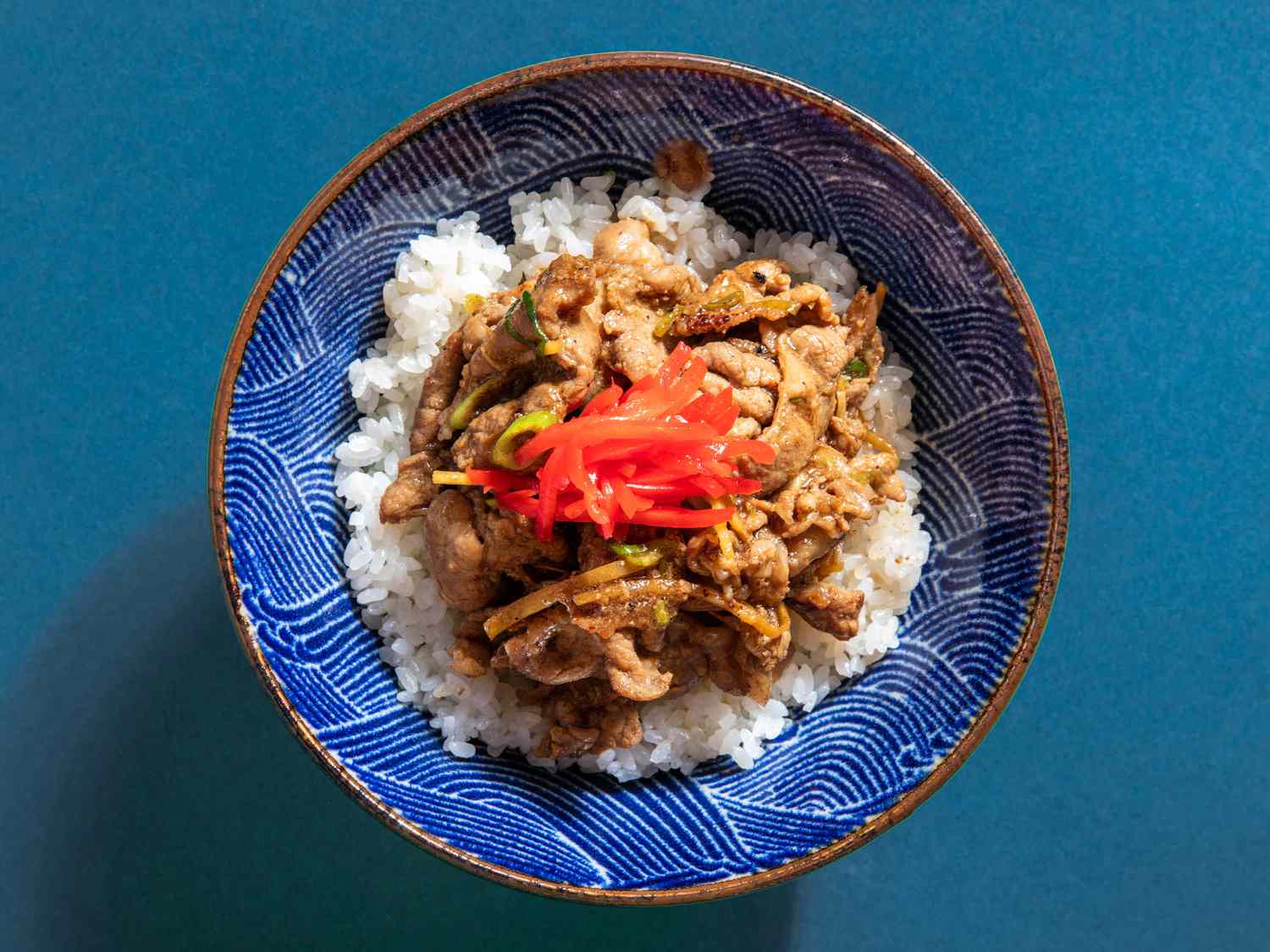 pork ginger over rice garnished with kizami shoga in a blue patterned bowl