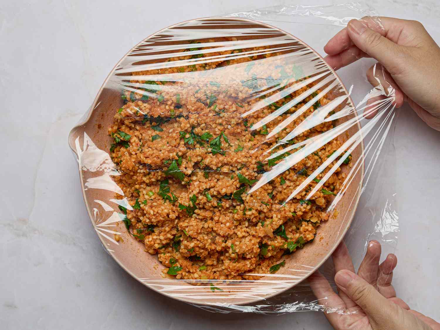 Hands covering a bowl of lentil salad with plastic wrap
