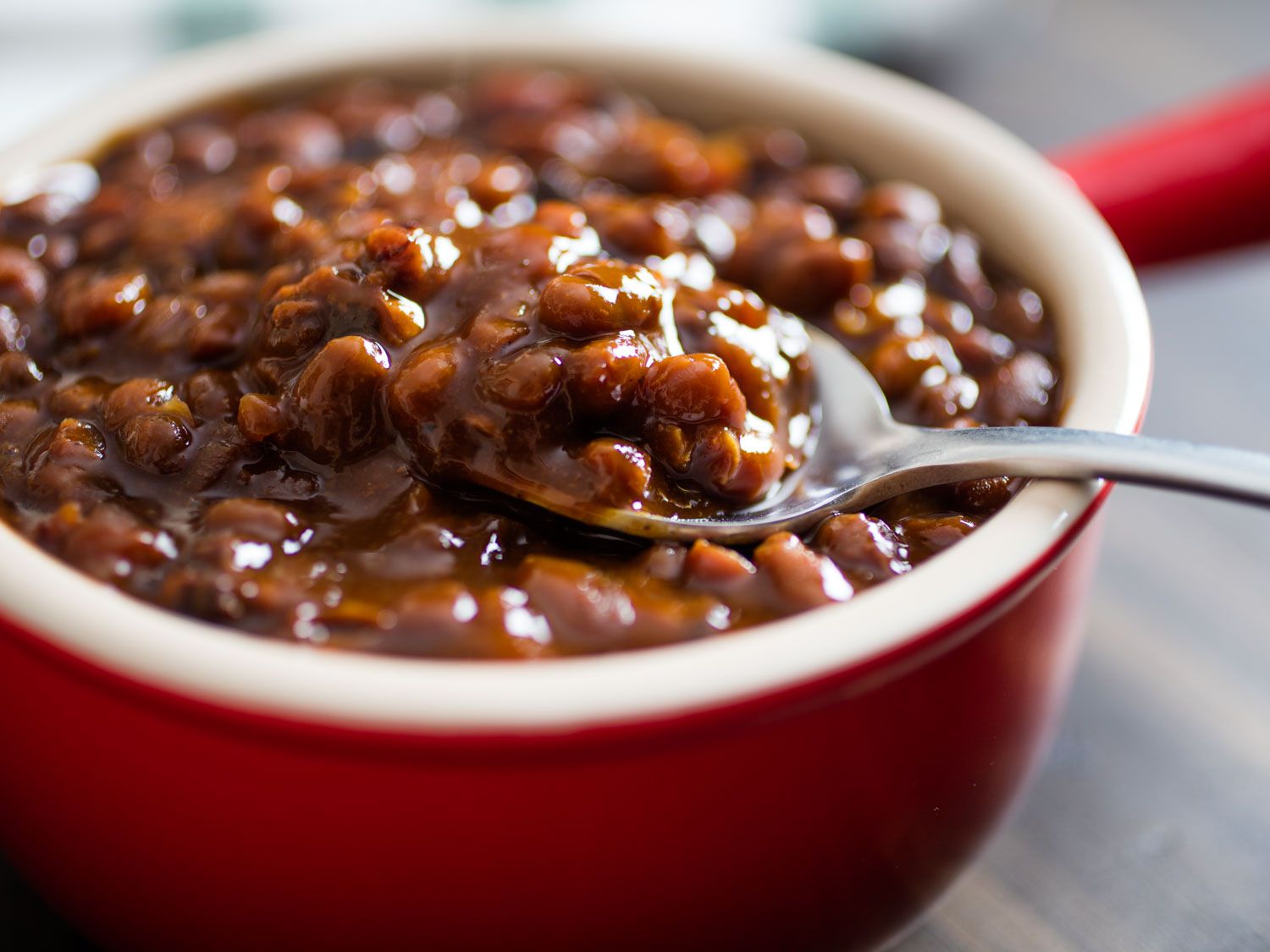 Scooping a spoonful of Boston baked beans from a small red crock.
