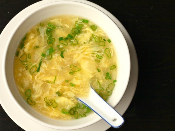 White bowl filled with simple Chinese egg drop soup, topped with scallions, on a dark background.