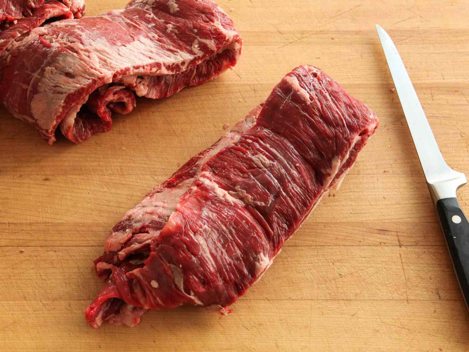 Skirt steak on a wooden cutting board next to a knife.
