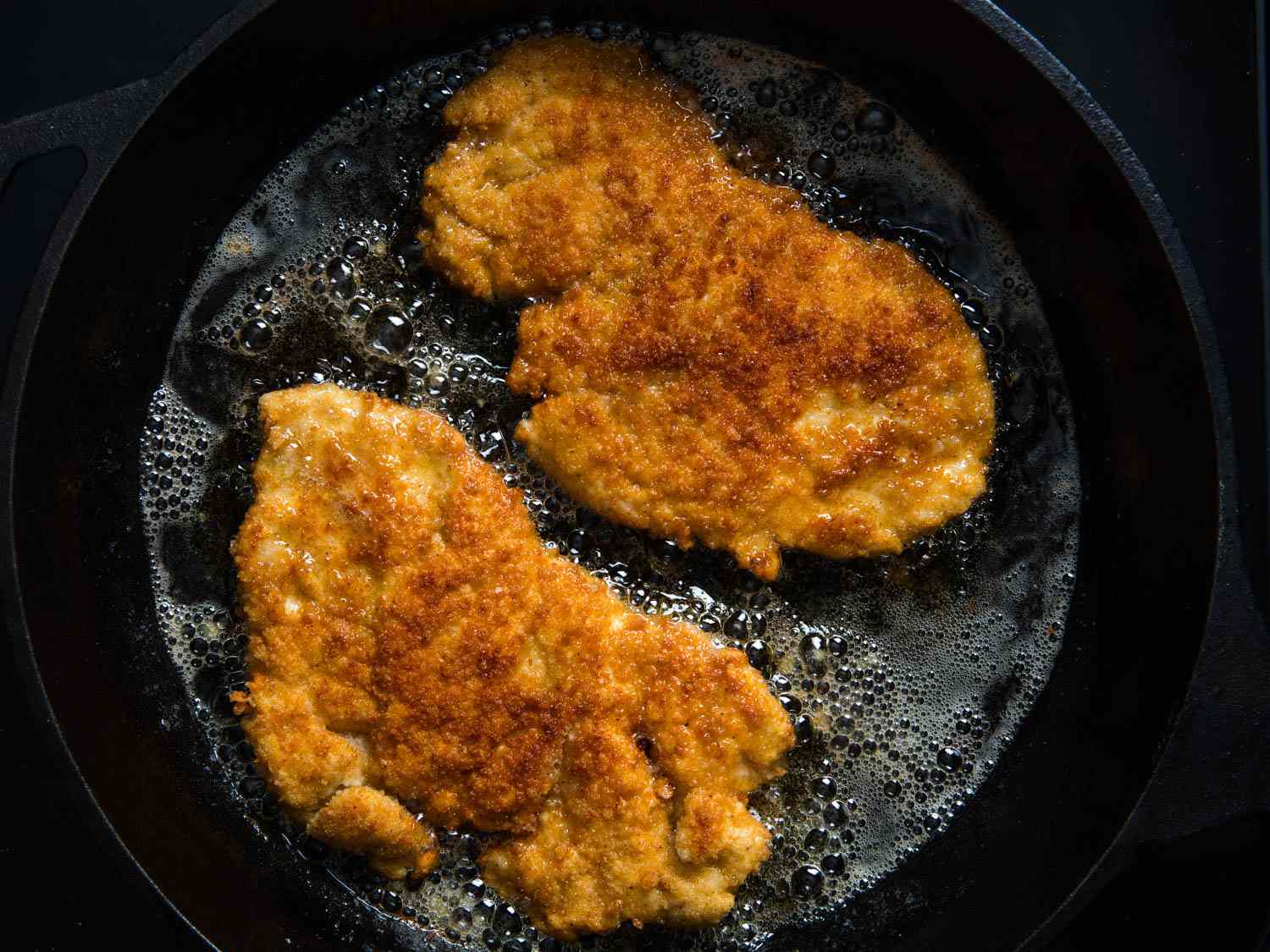 Overhead shot of the breaded cutlets frying in a cast iron skillet.
