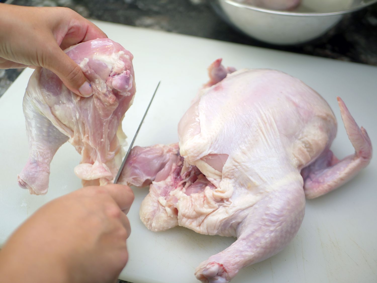 a person using a santoku knife to break down a whole chicken