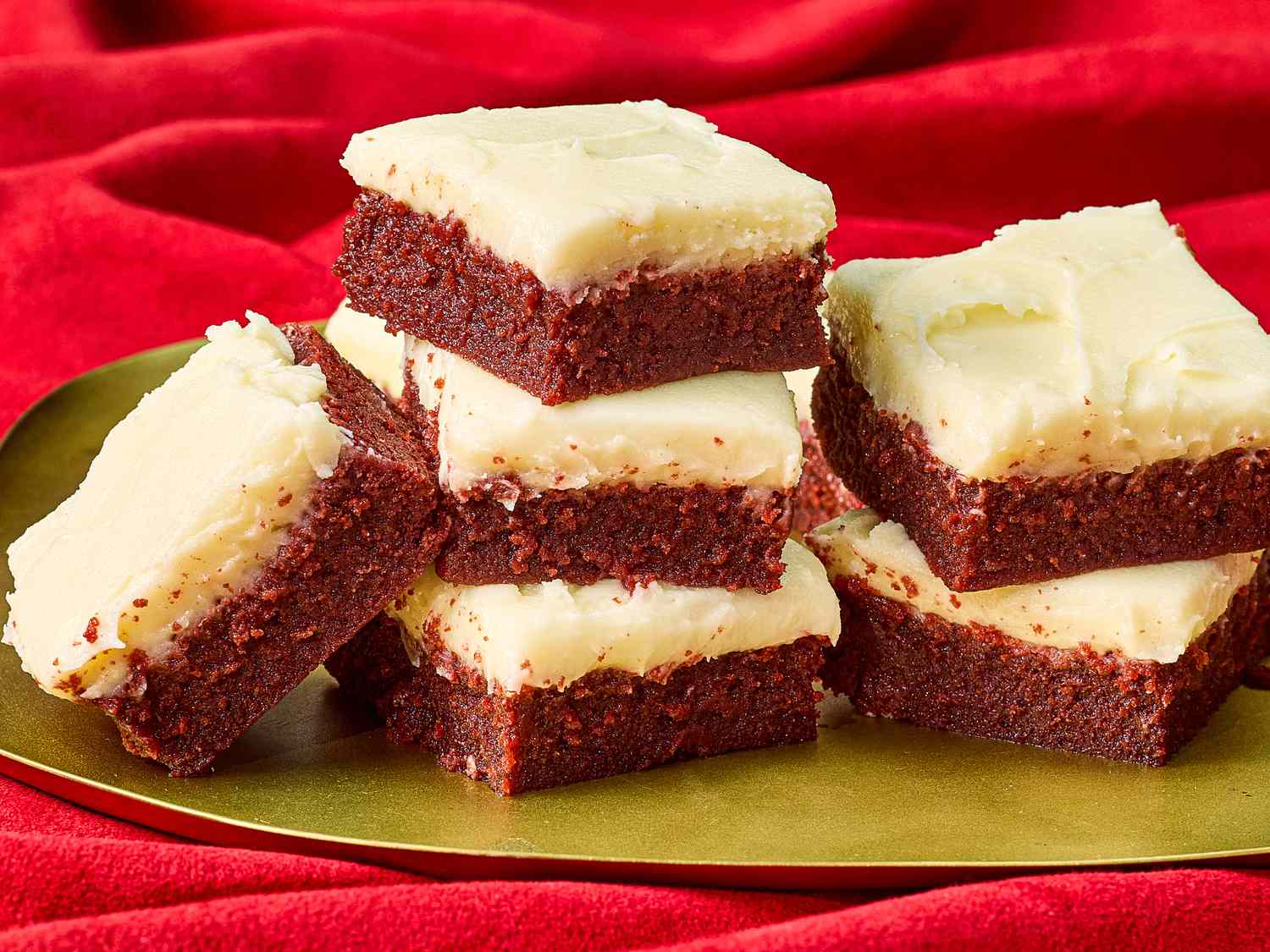 red velvet brownie squares stacked together on a gold platter on top of a red velvet backdrop