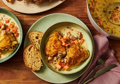 A plate of chicken served with vegetables and bread next to a bowl of soup