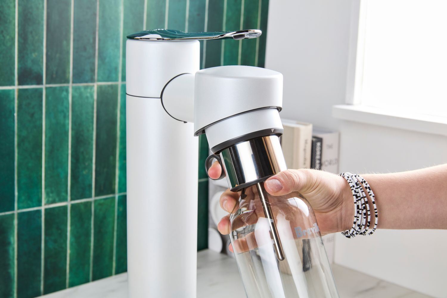 A hand holding a transparent bottle under a countertop carbonation appliance