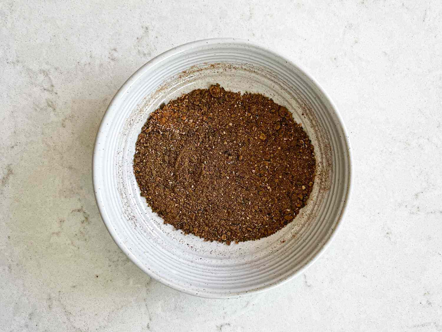 Allspice, cinnamon, black pepper, and nutmeg mixed in a small ceramic bowl.