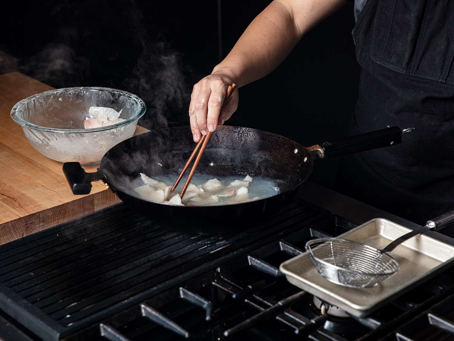 View from the side of a chef demonstrating the pass-through cooking technique