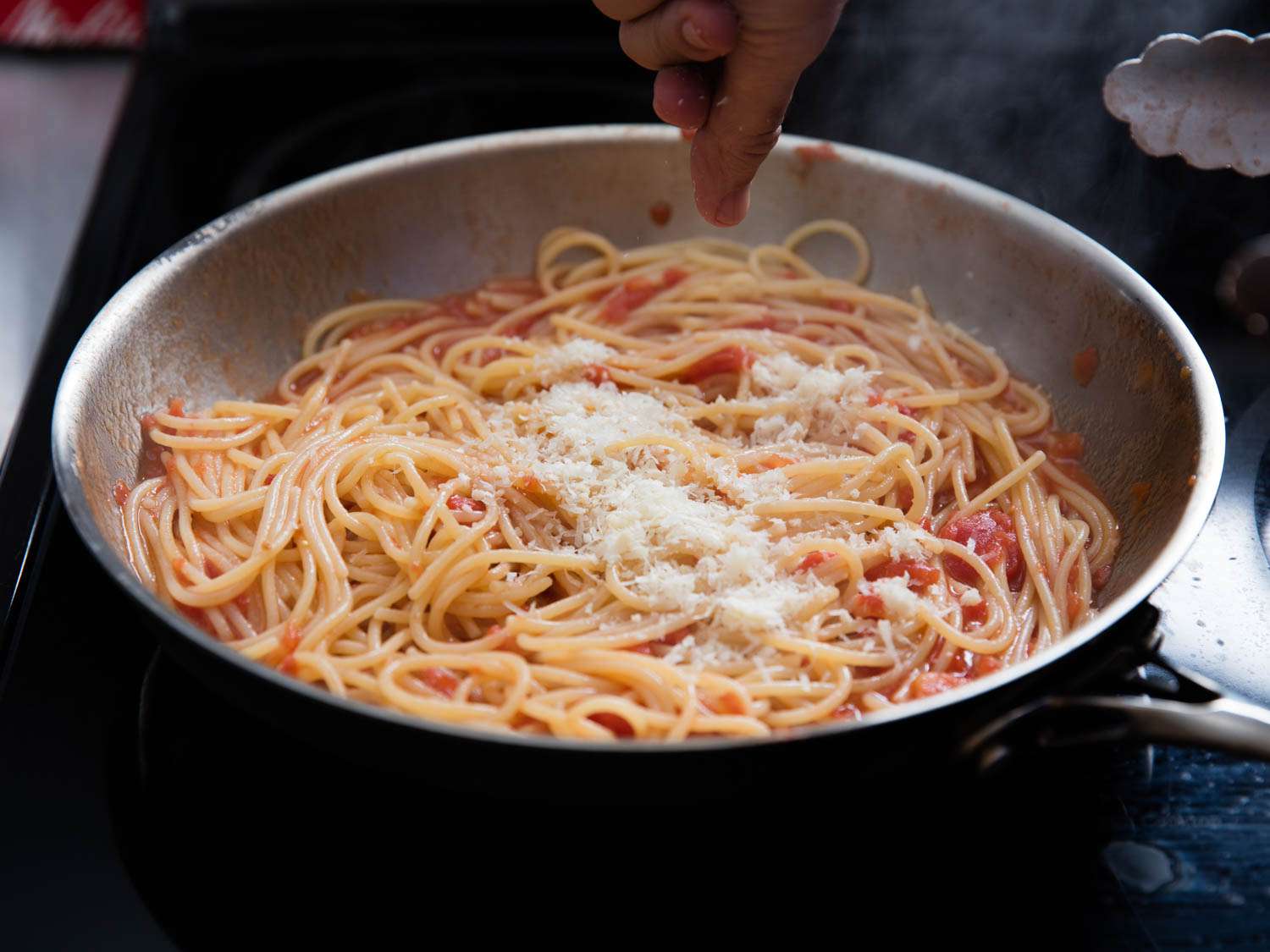 Grated cheese being sprinkled into the pasta and red pasta sauce mixture.