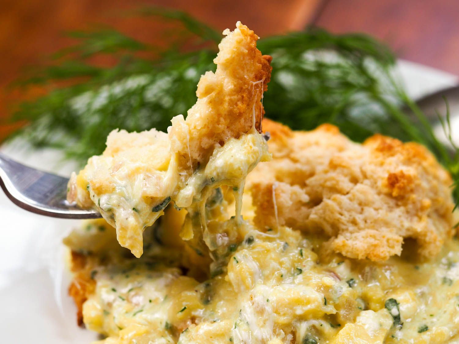 A fork digging into a scrambled egg drop biscuit sandwich.