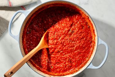 A pot of Italian-American tomato sauce in a dutch oven with a wooden spoon.