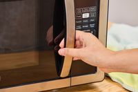 A hand holding the handle to the Farberware Countertop Compact Microwave (FMWO11AHTBKB) 
