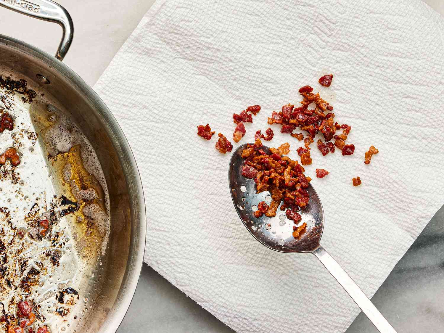 Fried bacon bits being spooned out of a skillet onto a paper towel 