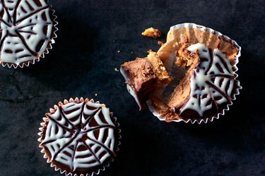 Overhead view of choclate mini cheese cakes. One cake has been partially devoured. Each cake has a spider-web pattern on top.