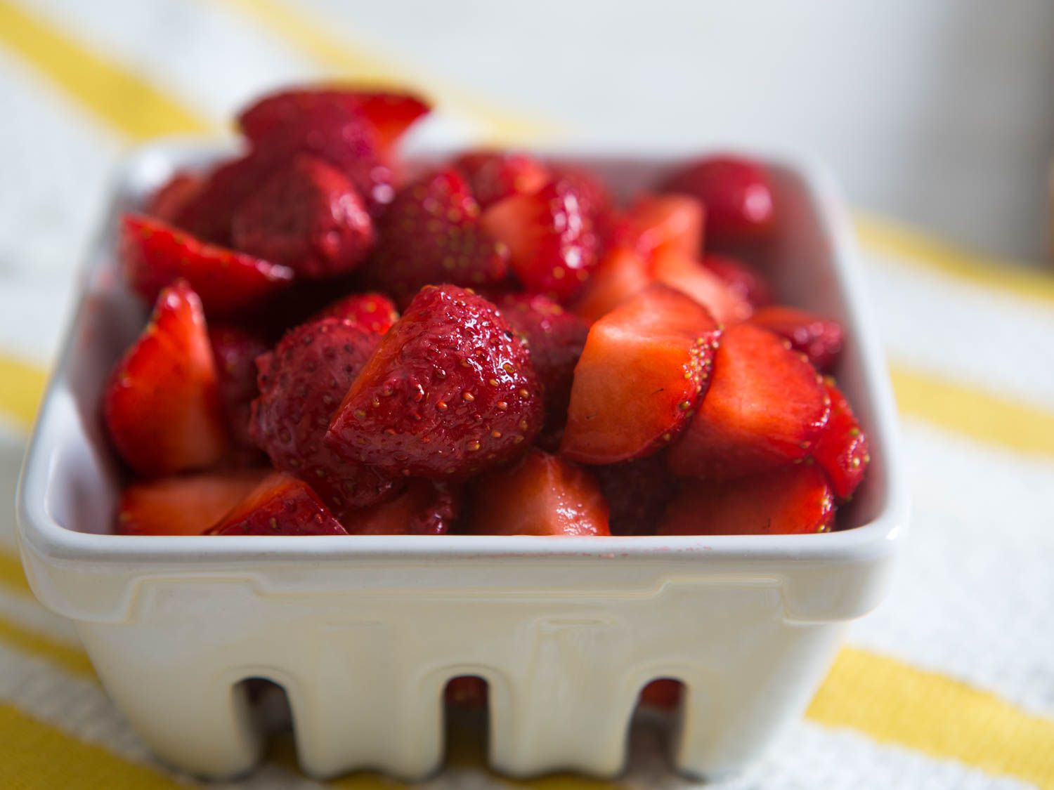 A closeup of a container of quartered fresh strawberries.