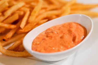 A small dish of sun-dried tomato and roasted garlic mayo next to a plate of French fries. 