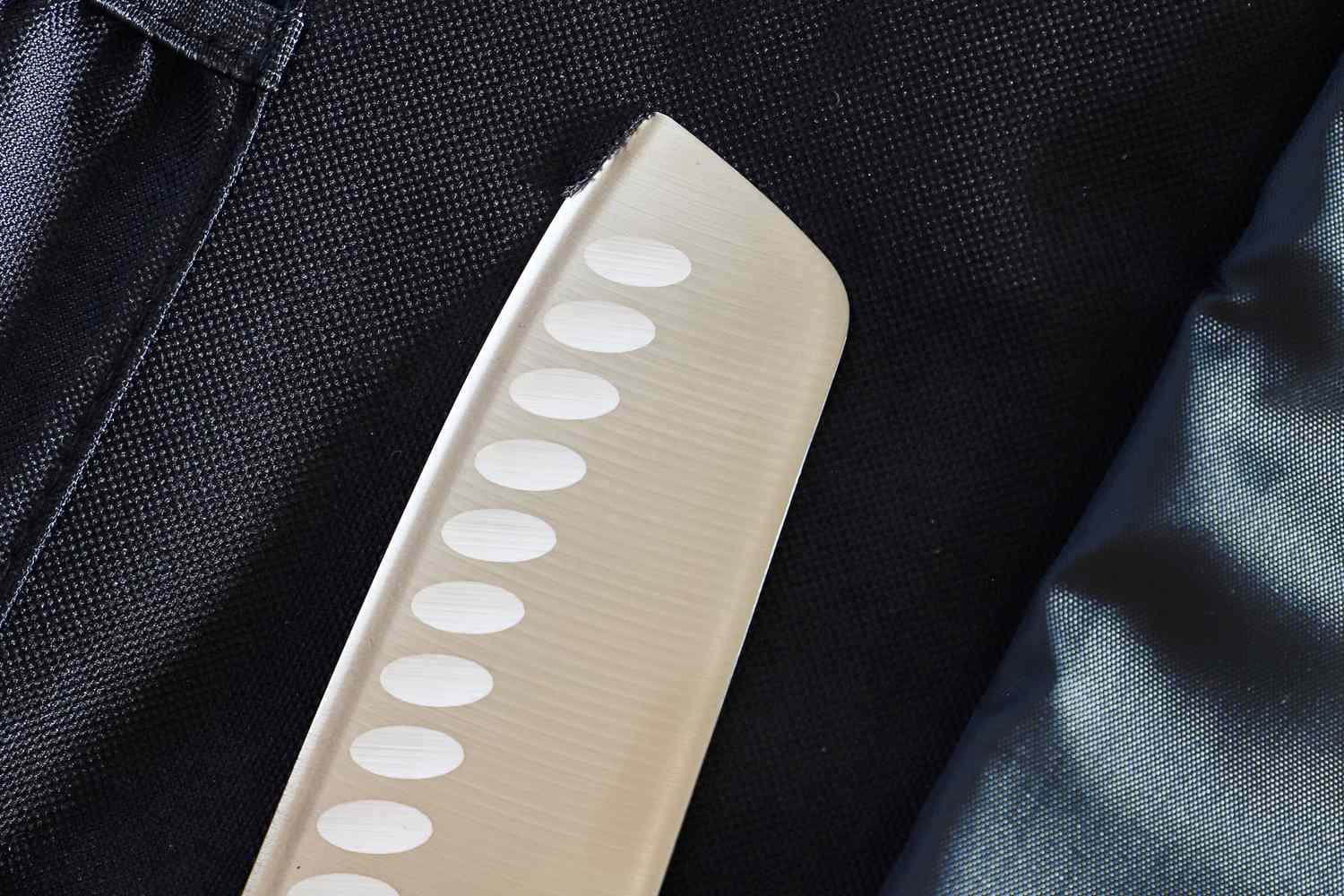Closeup of a knife blade with a textured handle againstAsaya Chef Knife Roll Bag