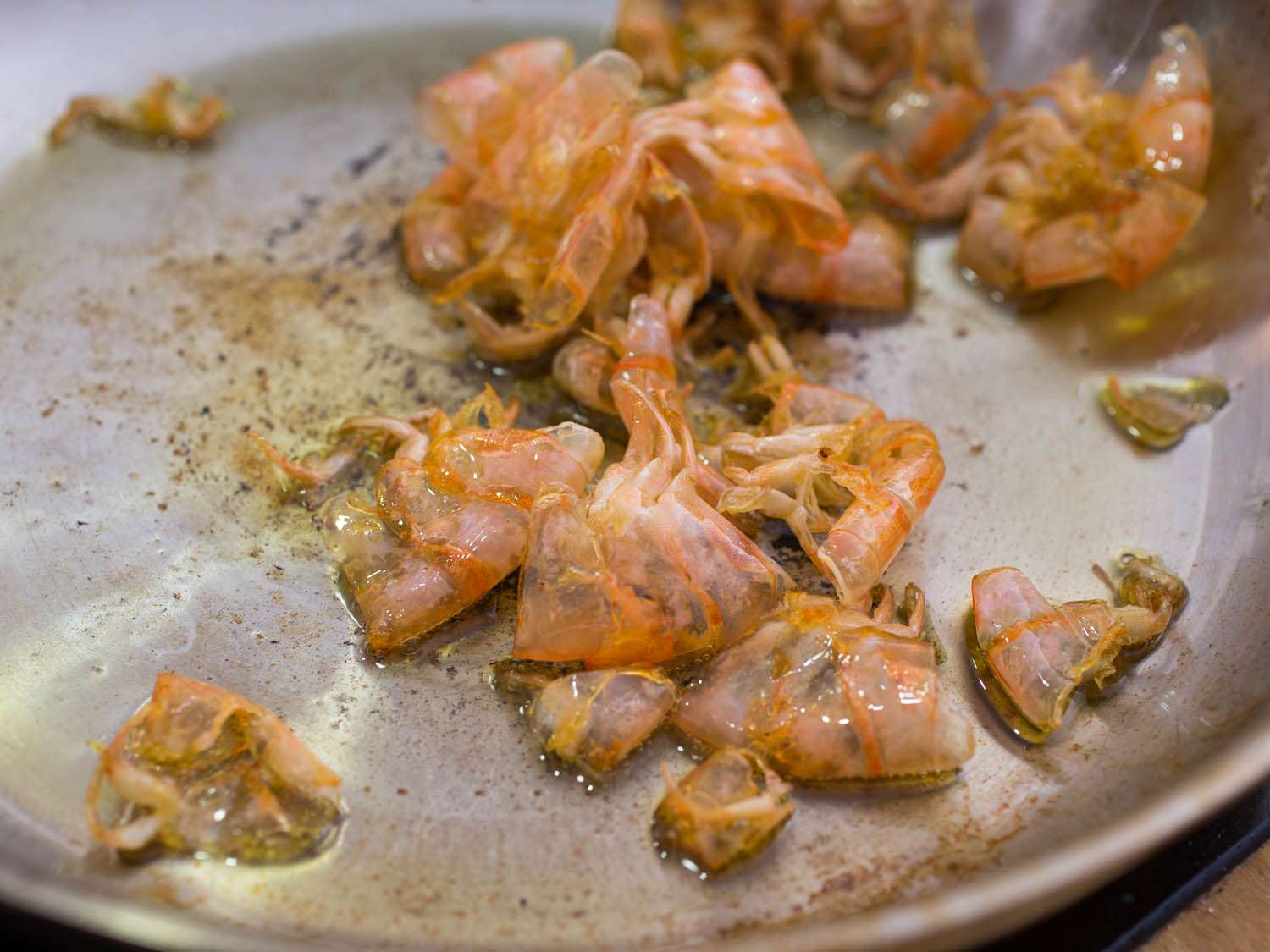 Shrimp shells in a skillet, sautéed in olive oil until caramelized.