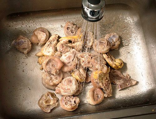 Washing blanched pork and chicken bones in a large, stainless steel sink.