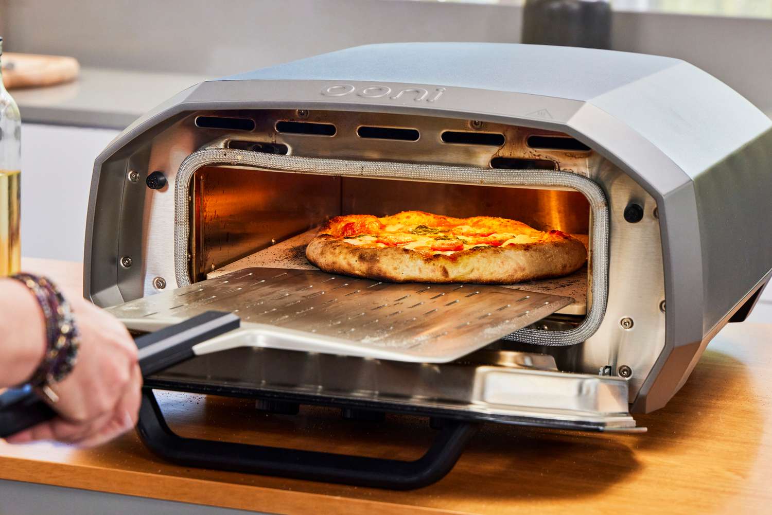 A person removes a pizza from the Ooni Volt 12 Electric Pizza Oven