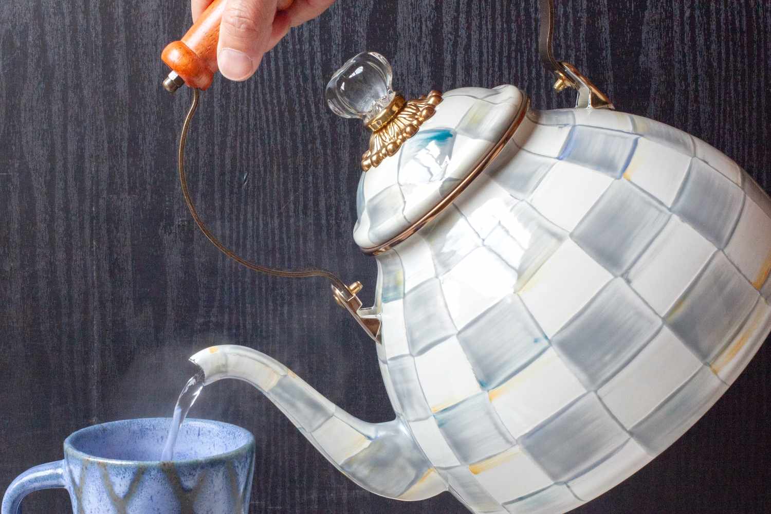 A hand pouring hot water from a teapot into a mug