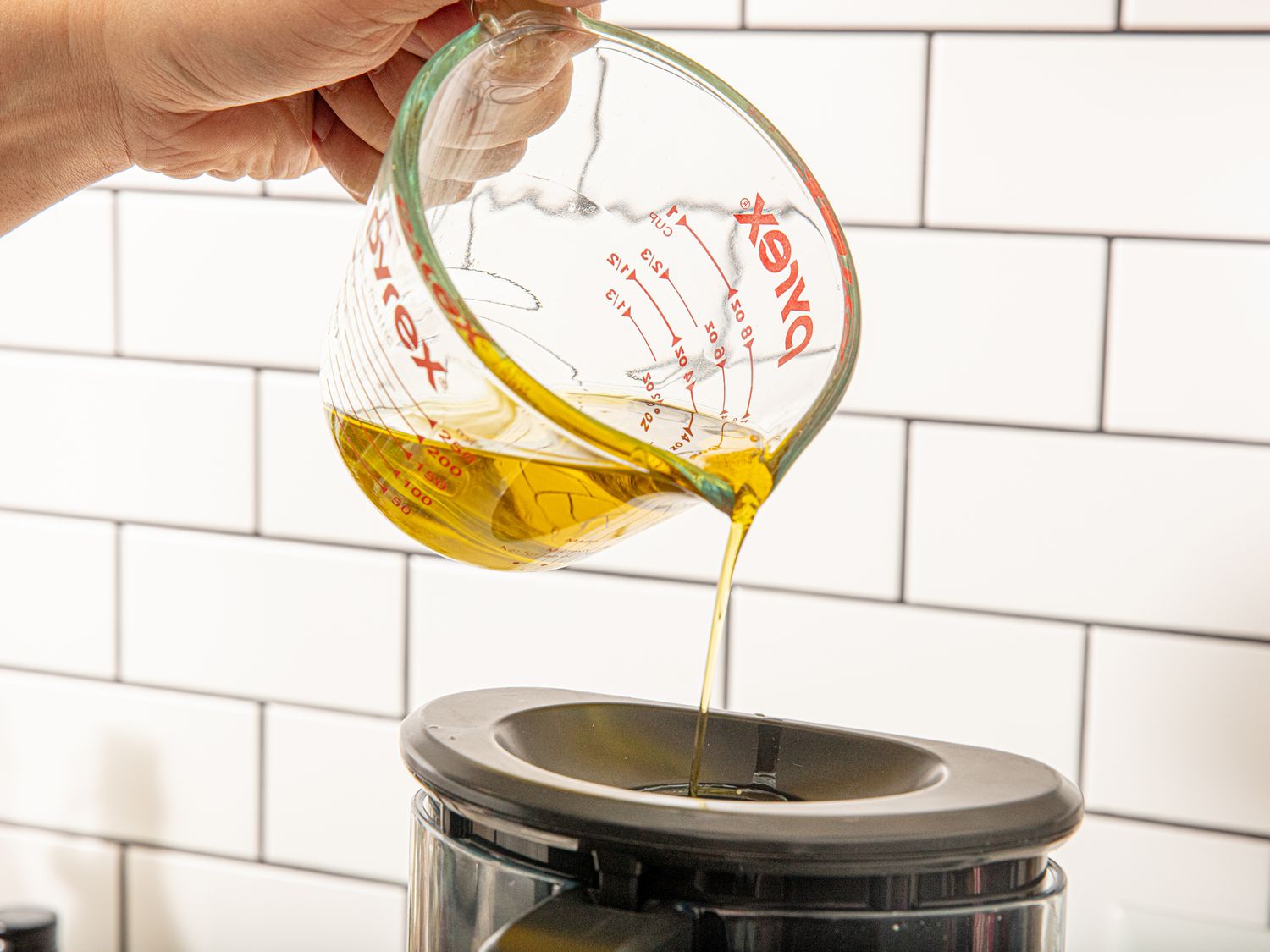Pouring oil from a measuring cup into a food processor