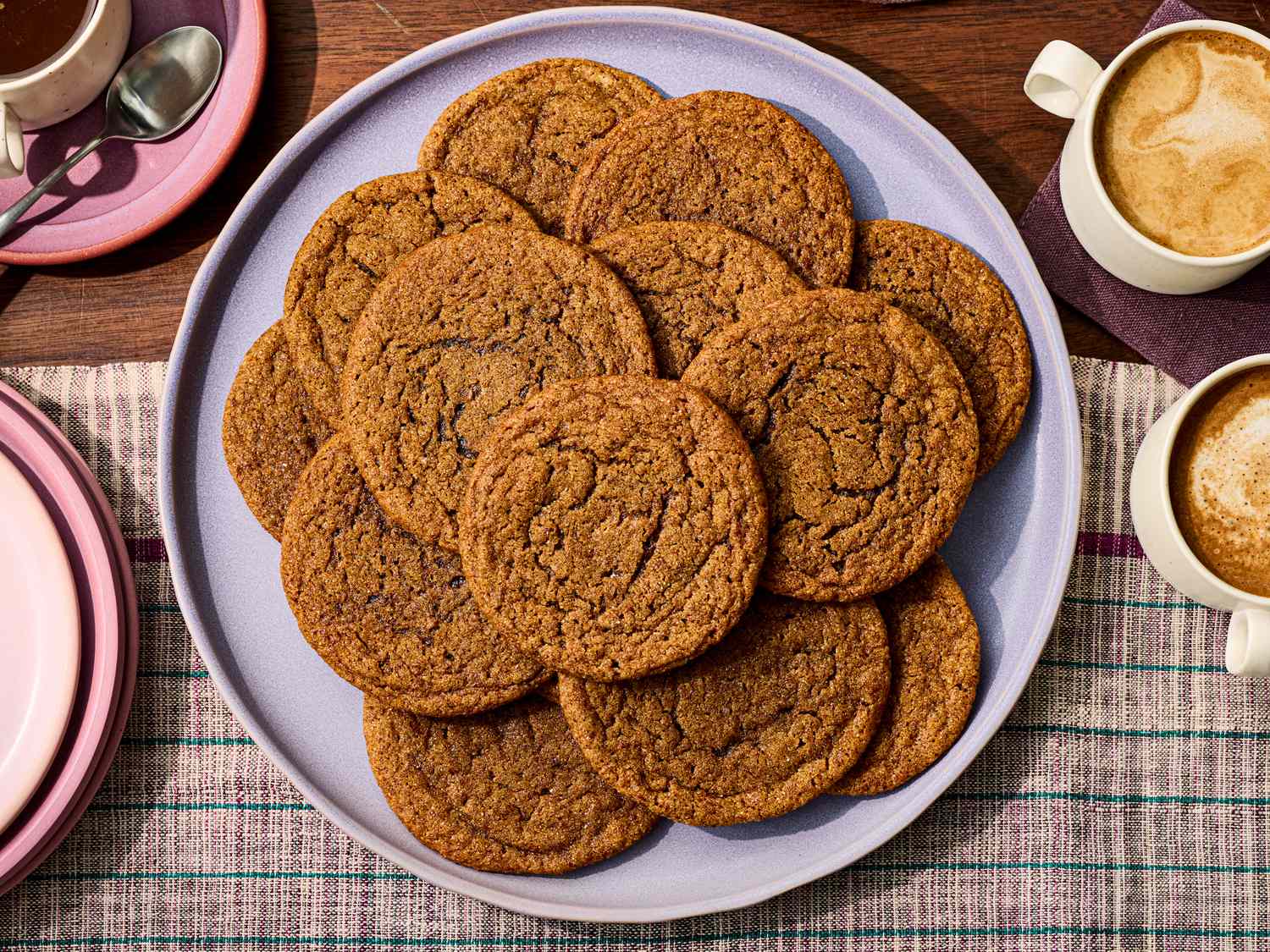 A plate of gingerbread cookies on a table setup with coffee mugs nearby