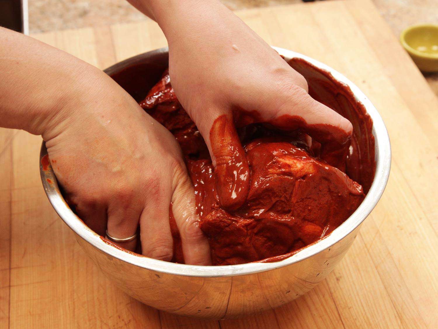Rubbing a raw pork shoulder in a bowl with a rub for cochina pibil. 