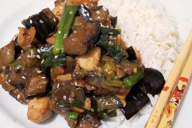 Closeup of sesame chicken and eggplant, served with white rice.