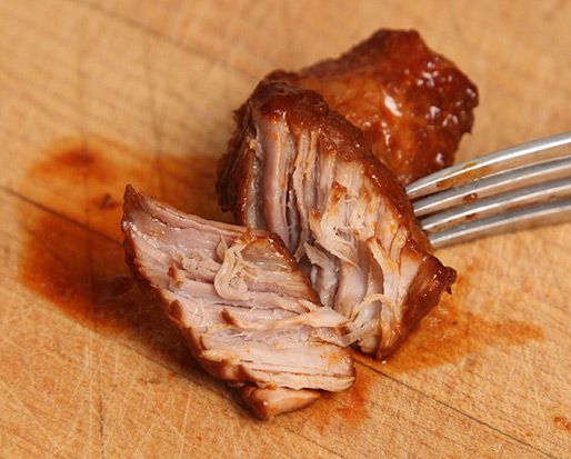 A chunk of braised pork from carne adovada, torn open with a fork to show the meat fibers inside. 