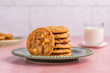 A plate of cookies with visible nuts, with a glass of milk in the background