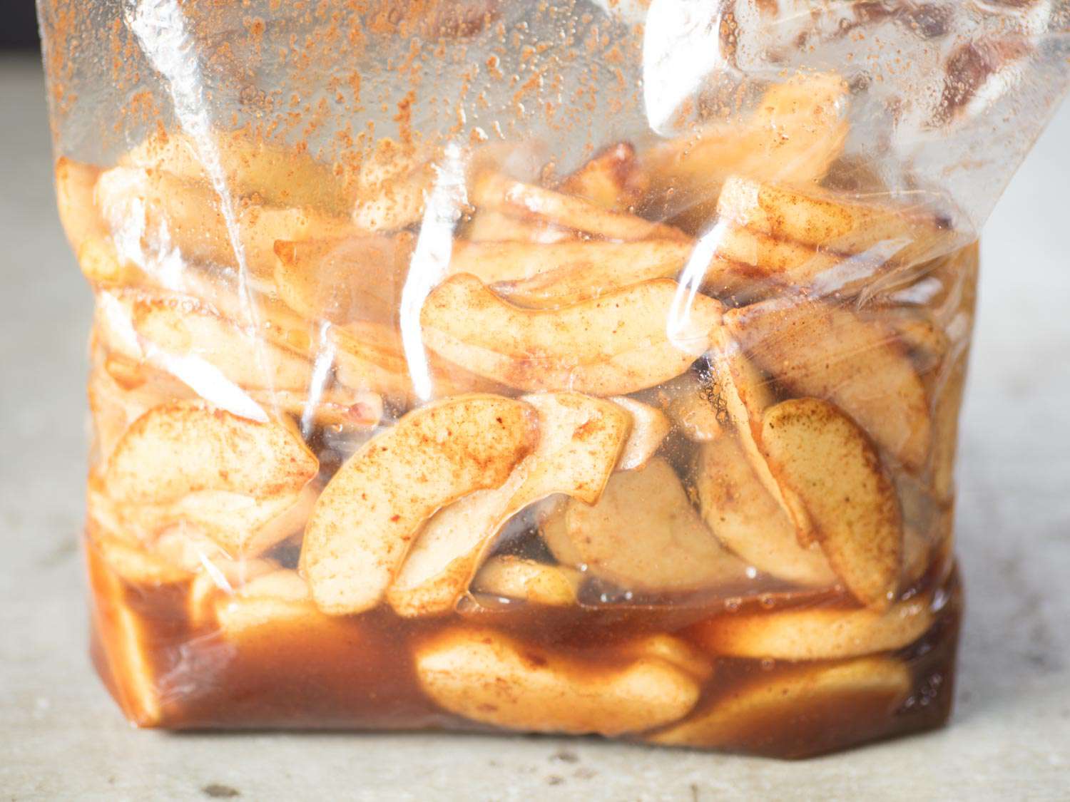 Apple slices macerating in a zip top bag, their liquid dissolving the brown sugar. 