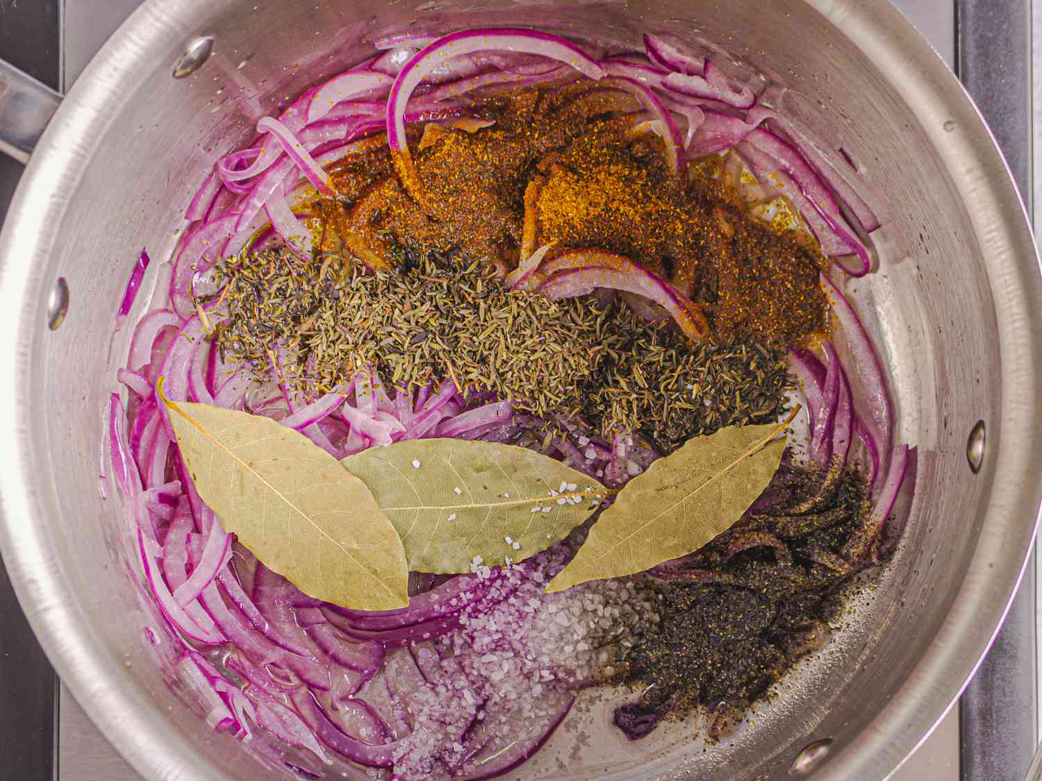 Overhead view of onions, bay leaves, cumin, seasoning and oil in pot