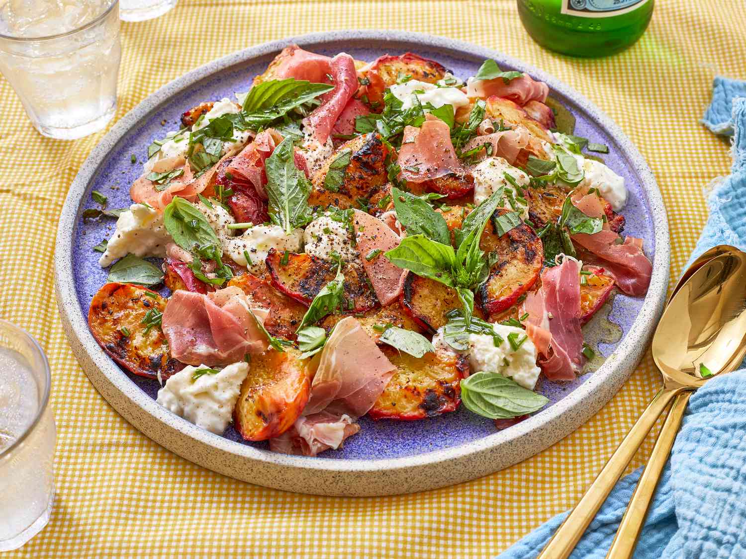 Gilled peach salad with burrata, prosciutto, and fresh herbs arranged on a blue plate
