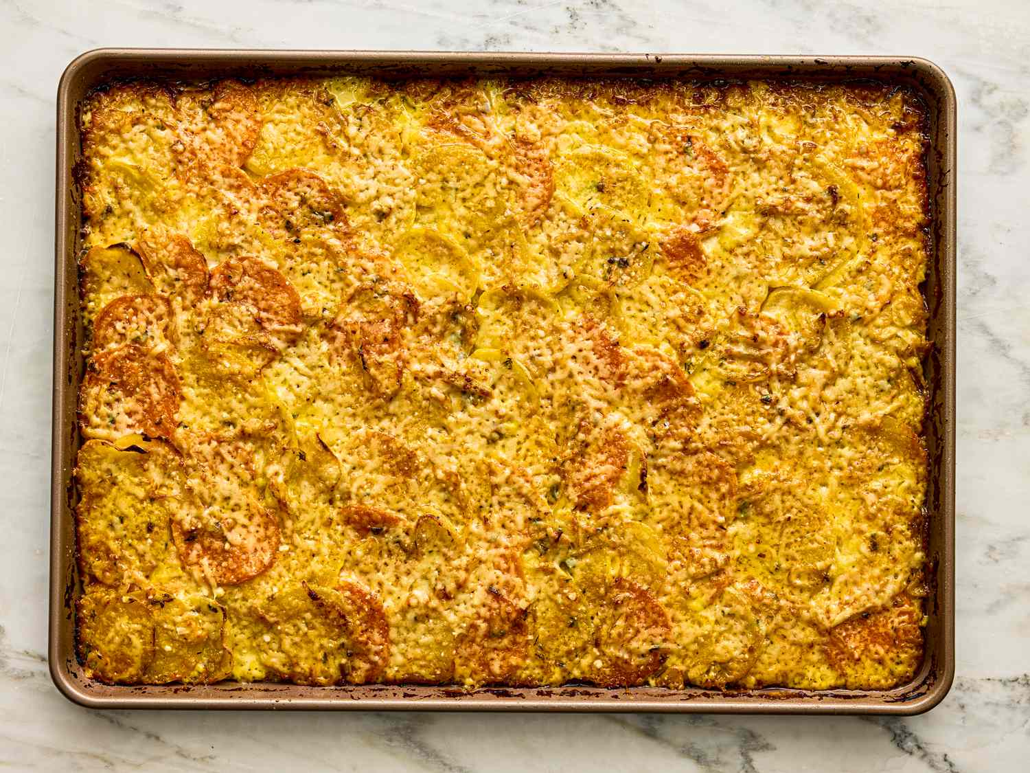 Baked root vegetable gratin on a sheet pan prepared with thinly sliced vegetables and a layering of cheese on top