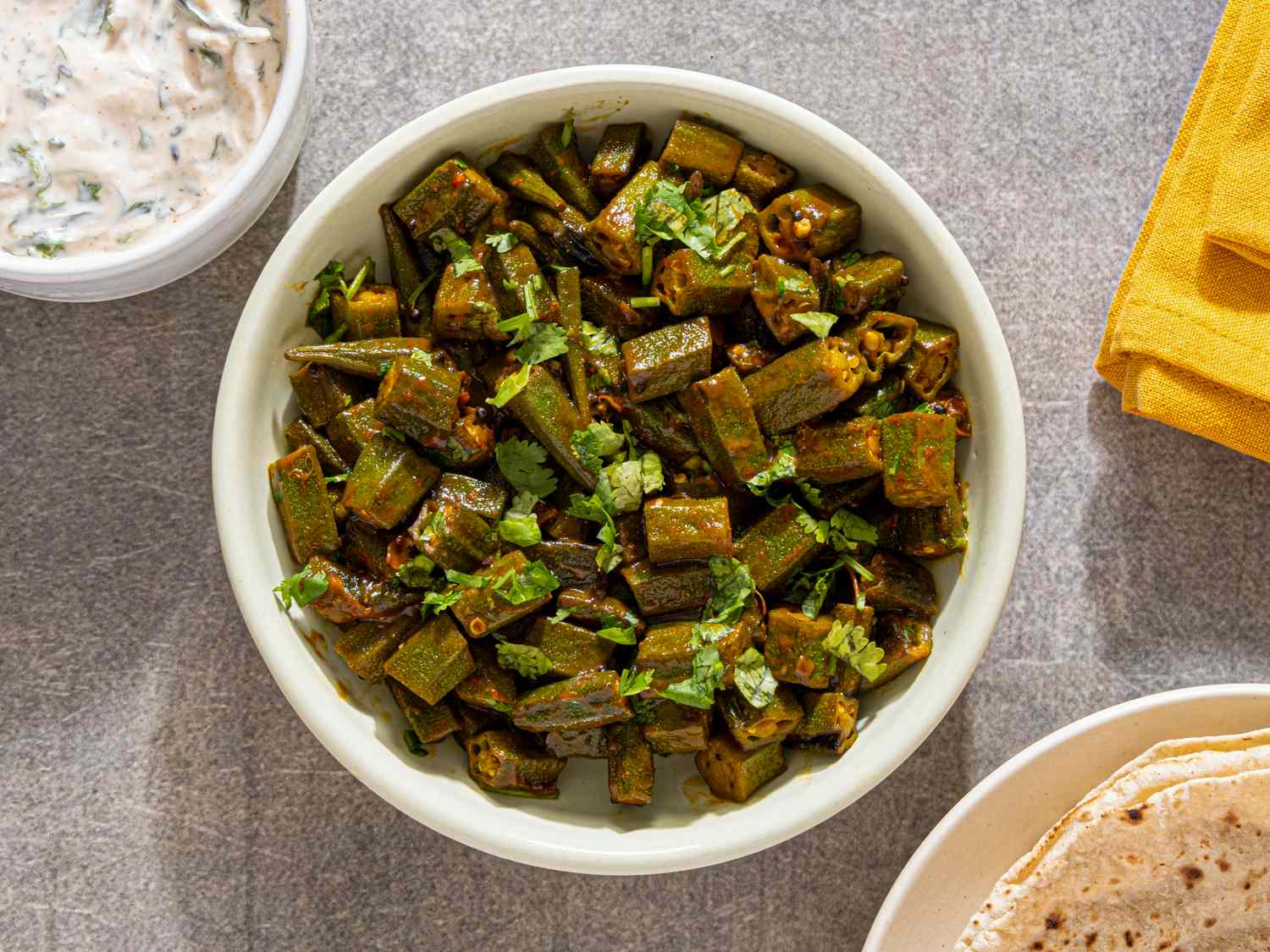 A bowl of spiced okra garnished with cilantro served on a table with side dishes