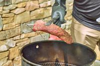A person cooks meat in the Pit Barrel Cooker Co. Classic Pit Barrel Cooker