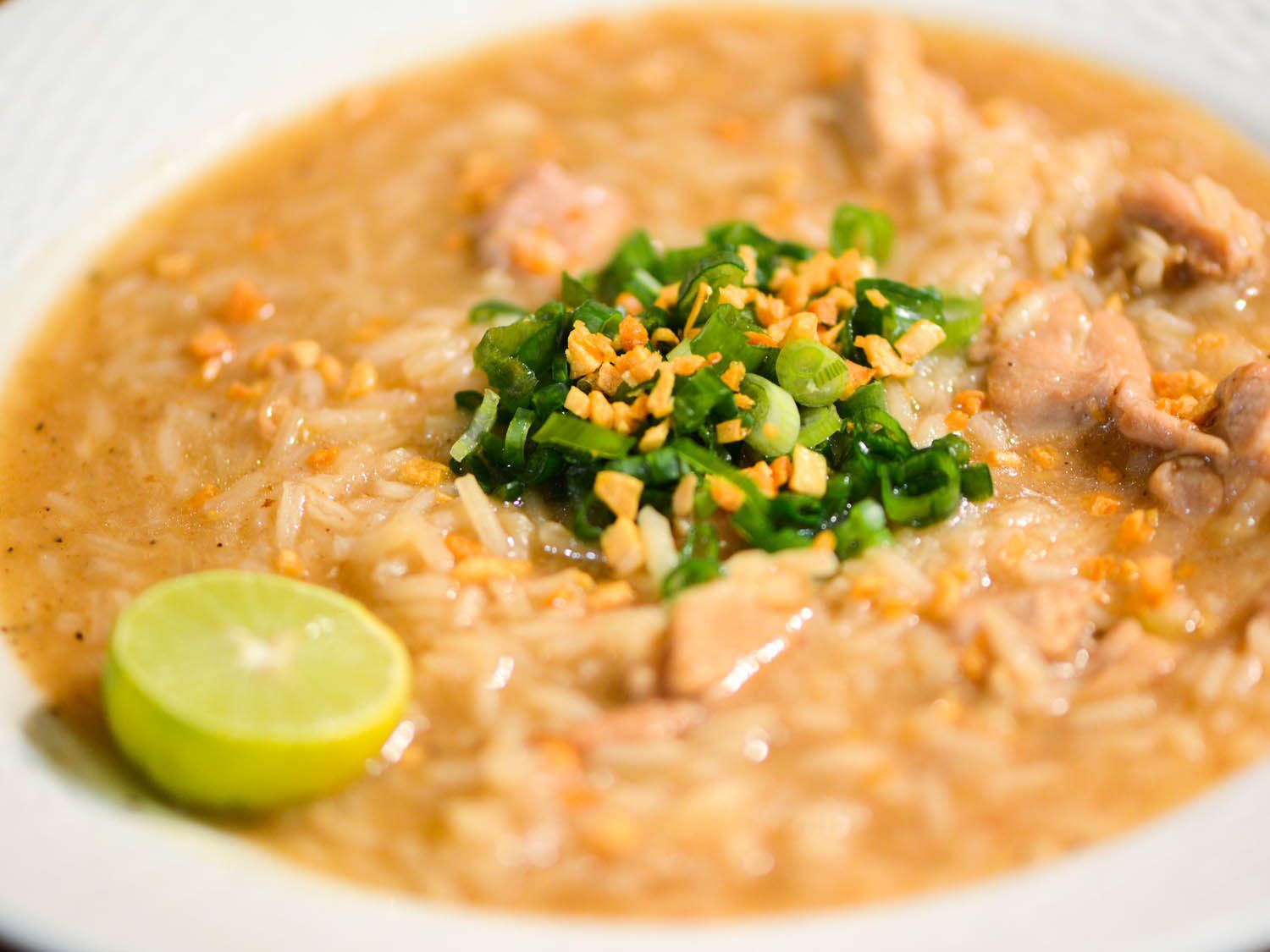A plated bowl of arroz caldo, garnished with half a lime and topped with fried garlic and thinly sliced scallion.