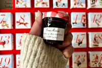 a hand holding a mini jar of Bonne Maman jar in front of the 2025 advent calendar