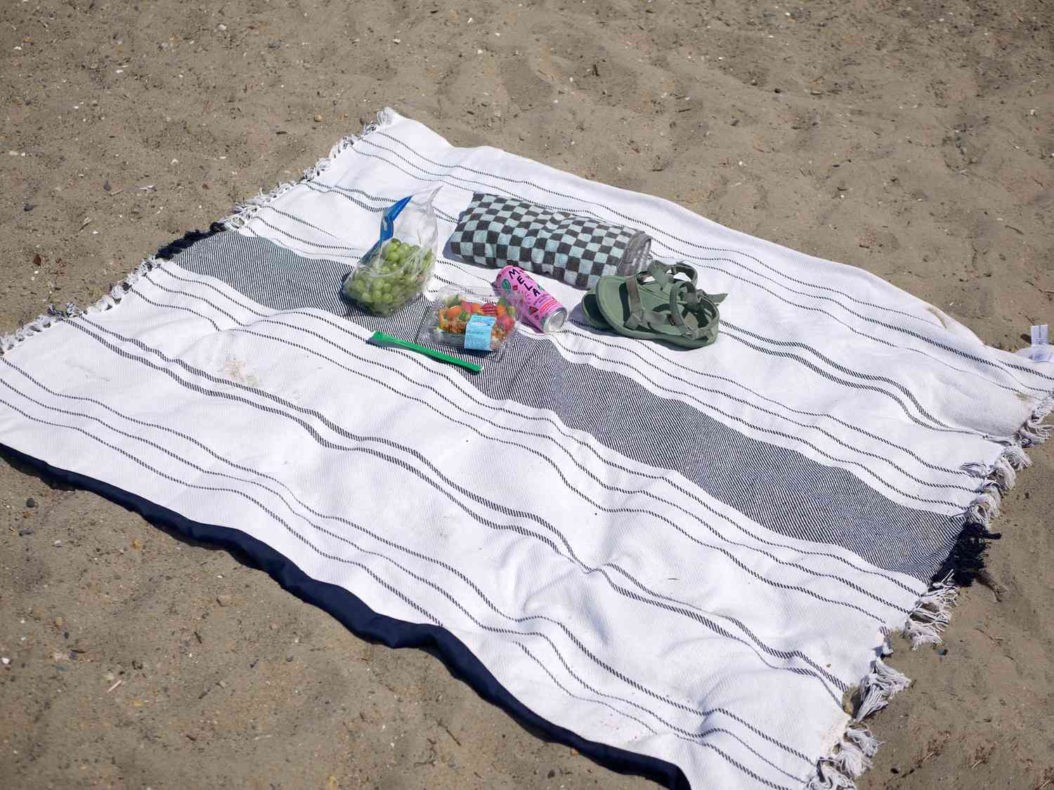 picnic time blanket on sand with sushi, grapes, watermelon juice, and a towel and sandals