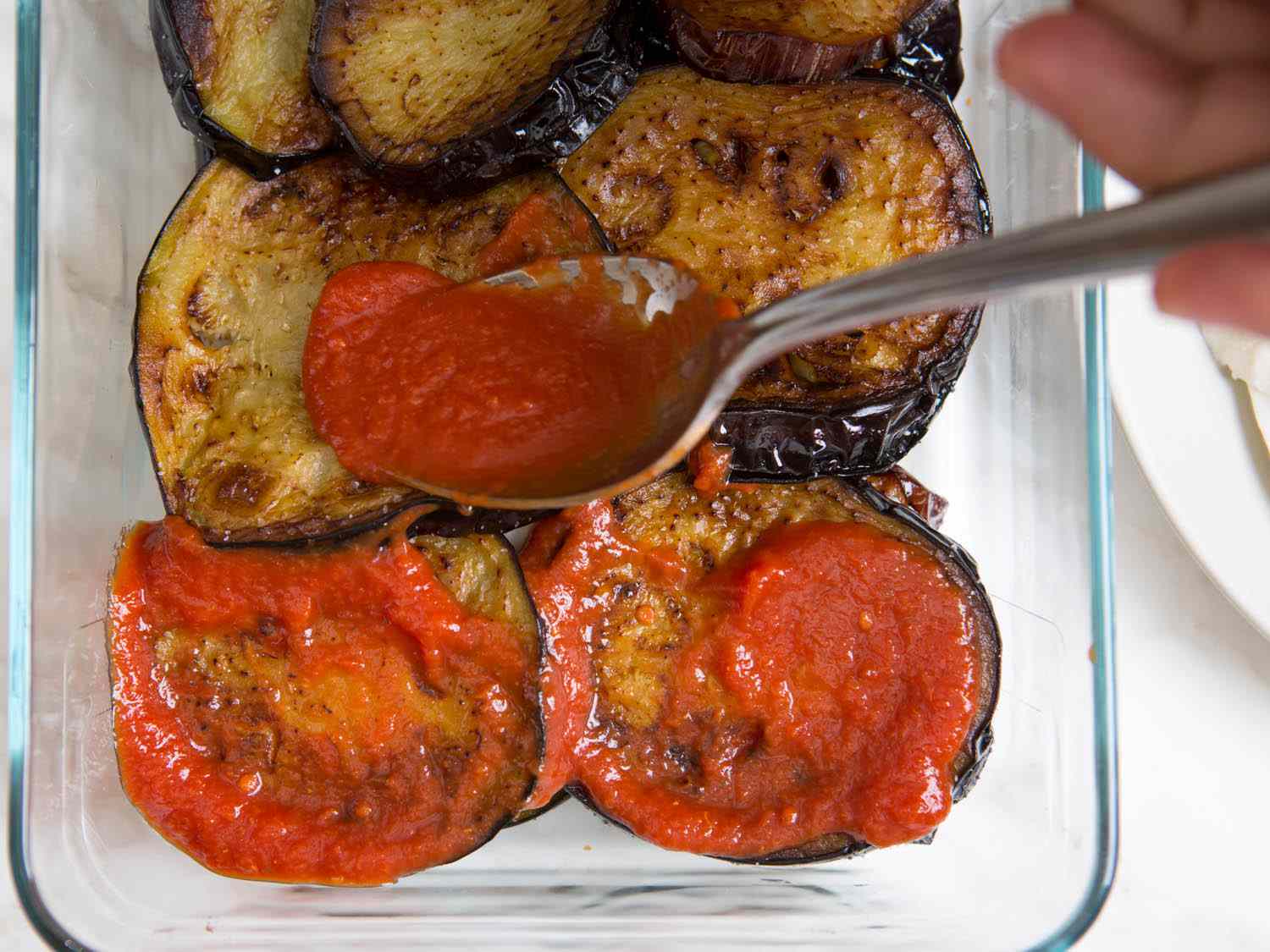 Spreading tomato sauce on top of fried eggplants for eggplant Parmesan. 