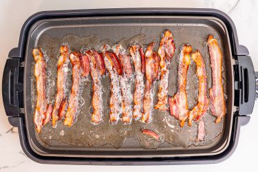 An electric griddle filled with bacon cooking.
