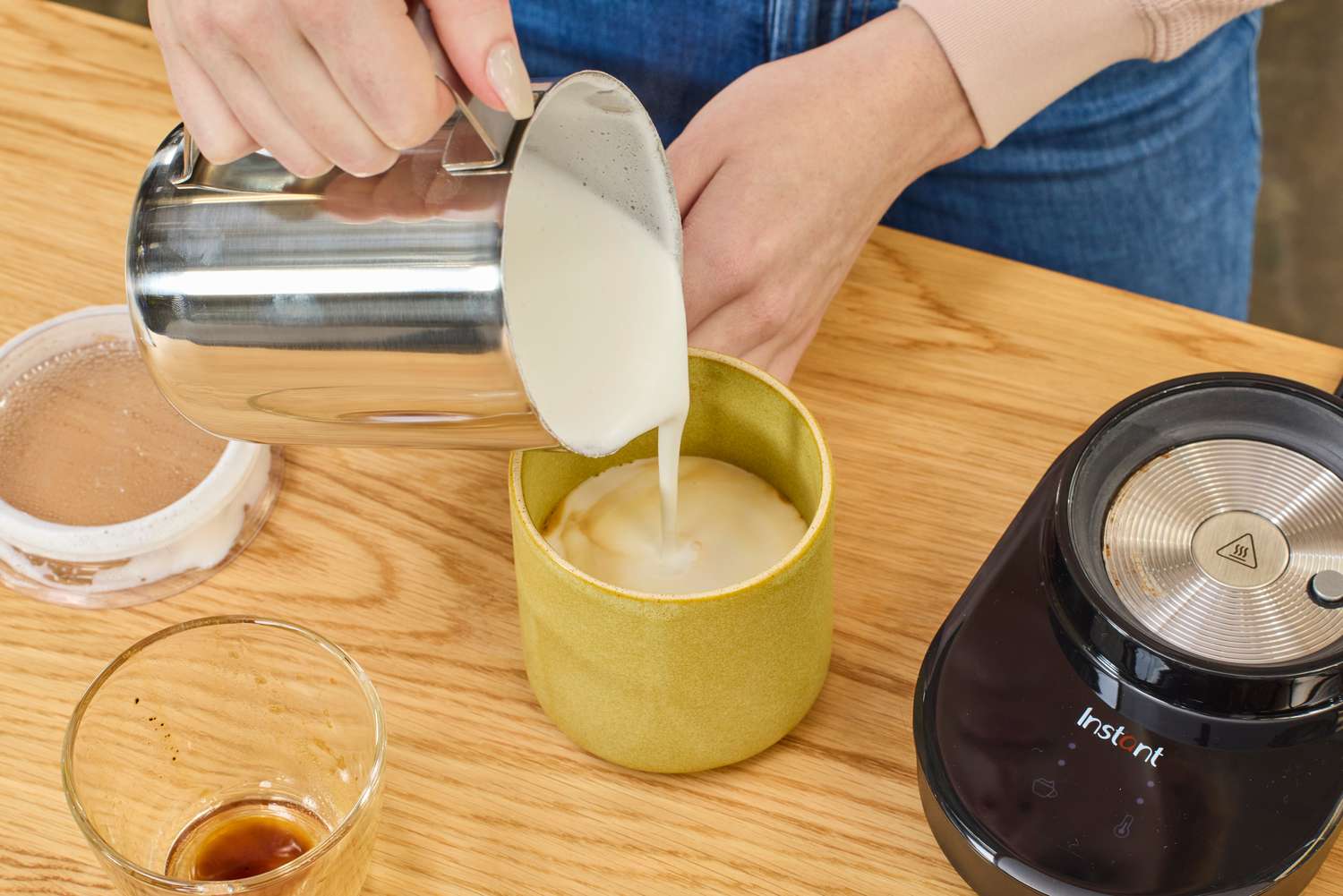 A person pouring frothed milk into a mug with coffee.