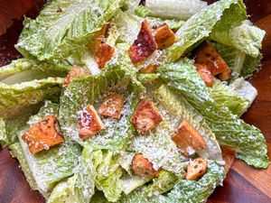 A Caesar salad with romaine lettuce croutons grated cheese served in a wooden bowl