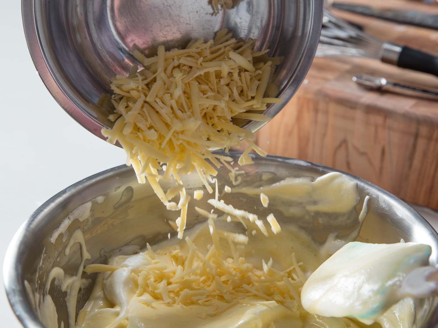 Adding grated cheese to the soufflé base.